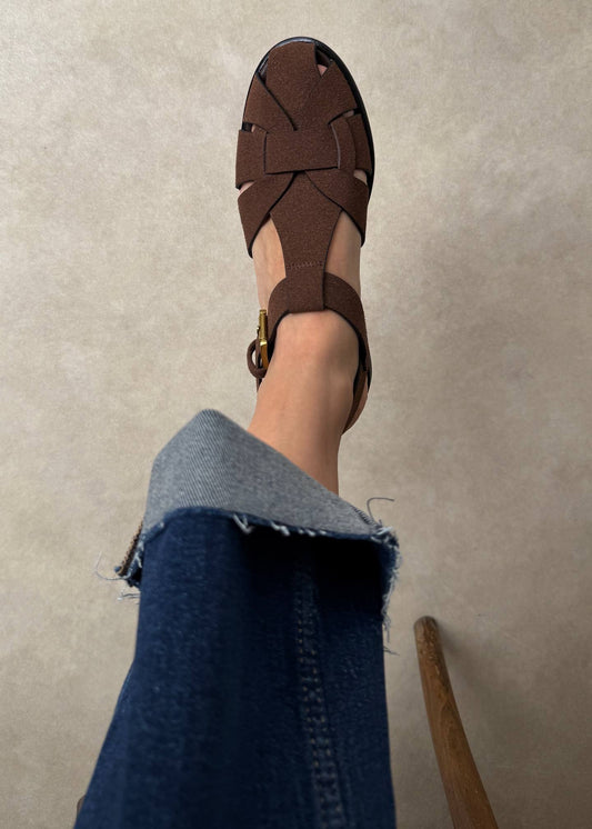 Brown sandal worn on a foot with a beige floor background
