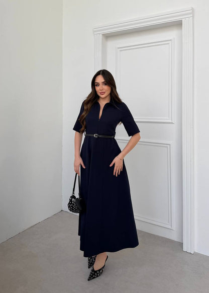 Woman in a navy dress standing in a minimalistic room with white walls and a door.