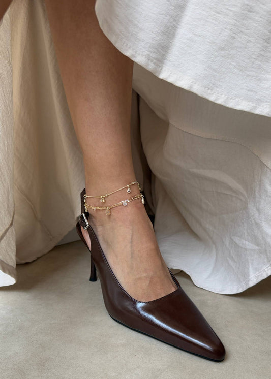 Brown high-heeled shoes worn with a white skirt on a neutral background