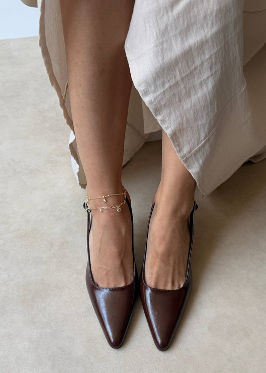 Brown pointed-toe shoes worn with a light-colored skirt on a neutral background
